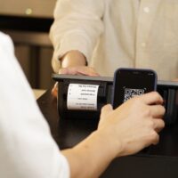 福岡の飲食店が公式LINEの友だち登録を増やすため、来店客にQRコードを案内しているカウンター越しのシーン